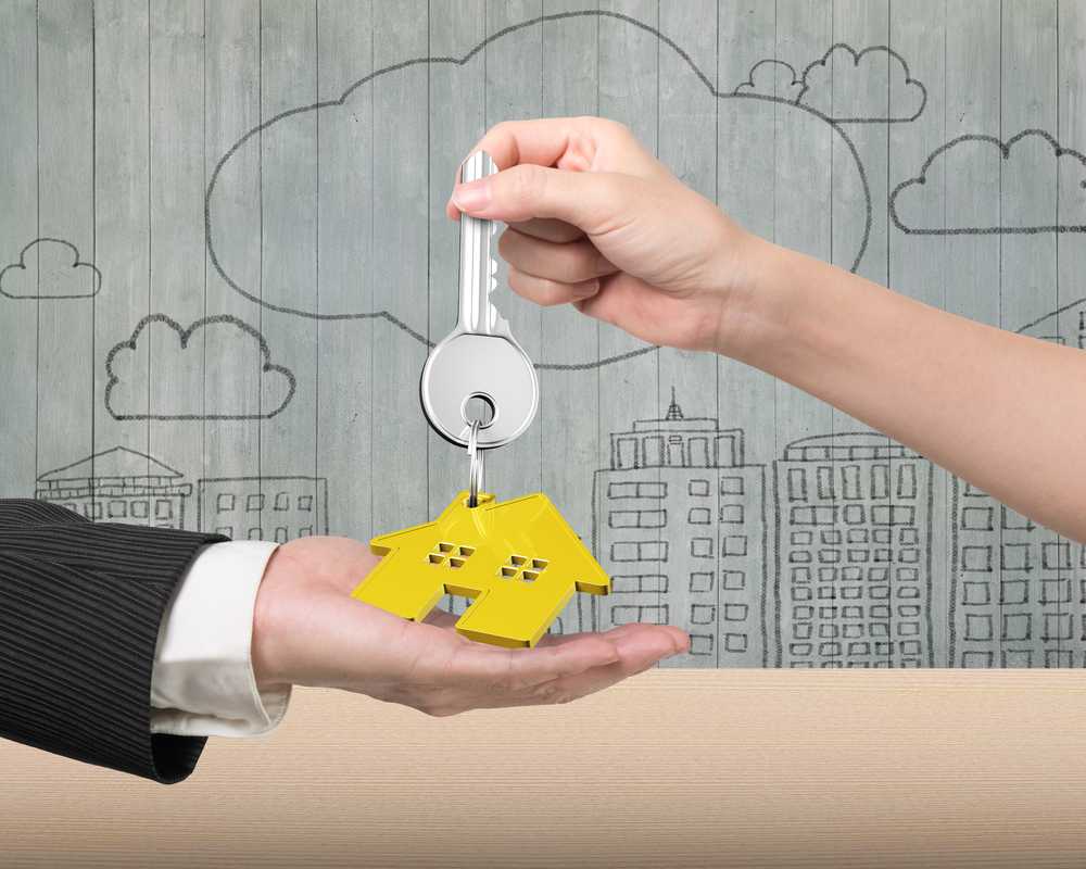 Woman hand giving silver key with gold house shape keyring to man hand, on doodles wooden wall background.