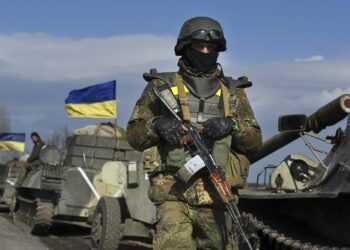 A Ukrainian serviceman stands guard as armored vehicles with canons in tow and with Ukrainian flags atop, stand on a road in the village of Fedorivka, eastern Ukraine, Friday, Feb. 27, 2015. Ukrainian and Russian-backed separatist forces have begun drawing back heavy weapons from the front line separating them in compliance with a cease-fire deal agreed in Belarus earlier in the month. (AP Photo/Evgeniy Maloletka)