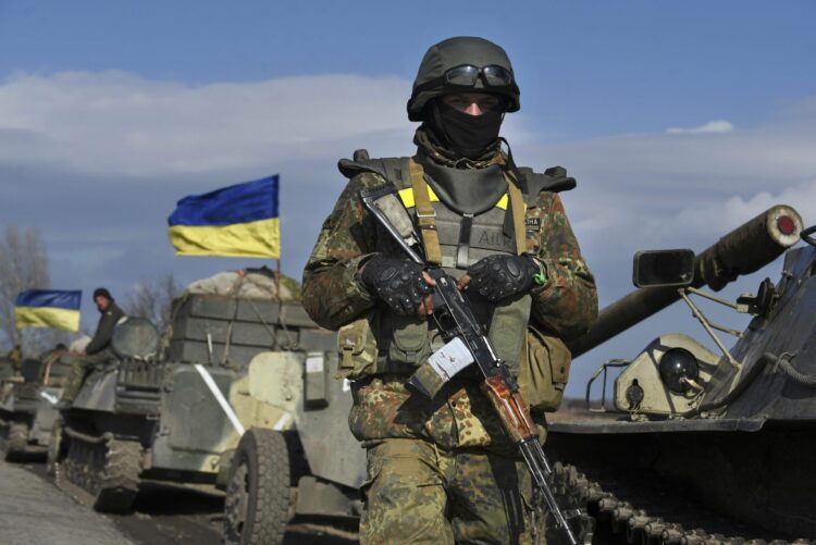 A Ukrainian serviceman stands guard as armored vehicles with canons in tow and with Ukrainian flags atop, stand on a road in the village of Fedorivka, eastern Ukraine, Friday, Feb. 27, 2015. Ukrainian and Russian-backed separatist forces have begun drawing back heavy weapons from the front line separating them in compliance with a cease-fire deal agreed in Belarus earlier in the month. (AP Photo/Evgeniy Maloletka)